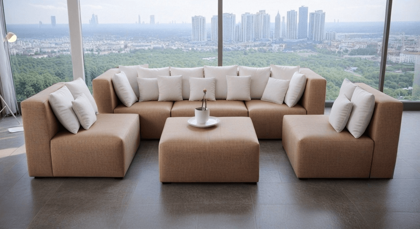 Nowoczesna, beżowa sofa narożna z wieloma białymi poduszkami w salonie z dużymi oknami z widokiem na miasto, oraz kwadratowa beżowa pufa służąca jako stolik - Holiday