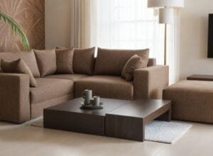 Nowoczesna, beżowa sofa modułowa z wieloma poduszkami, stolikiem kawowym i brązową pufą w minimalistycznym salonie - Rodos