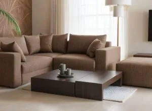 Nowoczesna, beżowa sofa modułowa z wieloma poduszkami, stolikiem kawowym i brązową pufą w minimalistycznym salonie - Rodos