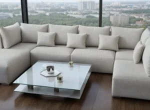 Duża, jasnoszara sofa narożna z leżanką i wieloma poduszkami, ustawiona w nowoczesnym salonie z panoramicznymi oknami z widokiem na miasto i zalesiony krajobraz. Przed sofą stoi szklany stolik kawowy z tacą i świeczkami - New Holiday